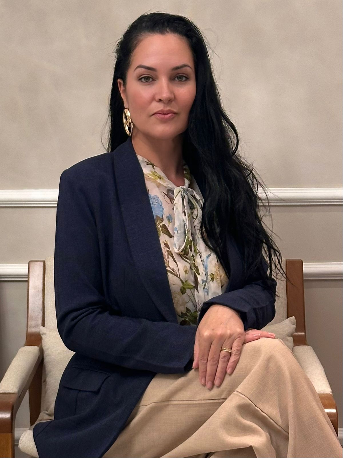 Dra. Vivianni Gil sentada em poltrona, com blazer azul-marinho